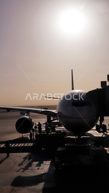 صورة لطائرة في المطار تستعد لتحميل الركاب بمطار الملك خالد في مدينة الرياض بالمملكة العربية السعودية ، الإستعداد للسفر ، سياحة وسفر ، وسائل النقل ، السفر والتنقل ، الطيران الجوي ، صورة جمالية لسماء السعودية وقت شروق الشمس