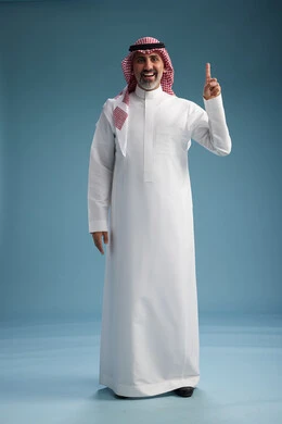 A portrait of a confident Arab Saudi Gulf man wearing a white thobe and a shemagh, smiling, with various gestures and movements, against a blue background.