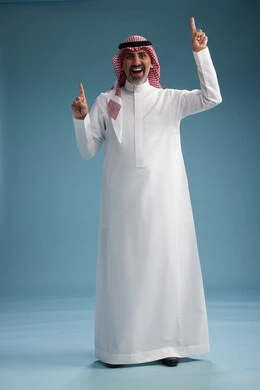 A portrait of a confident Arab Saudi Gulf man wearing a white thobe and a shemagh, smiling, with various gestures and movements, against a blue background.
