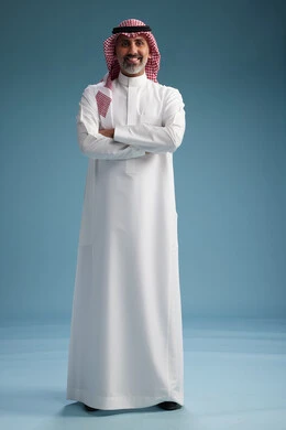 A portrait of a confident Arab Saudi Gulf man wearing a white thobe and a shemagh, smiling, with various gestures and movements, against a blue background.