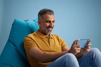 A portrait of an Arab Saudi Gulf man wearing casual attire sitting on a chair among blue flowers, with various gestures and movements, against a blue background.