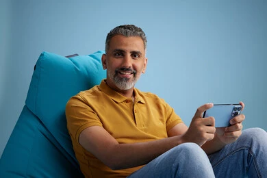A portrait of an Arab Saudi Gulf man wearing casual attire sitting on a chair among blue flowers, with various gestures and movements, against a blue background.