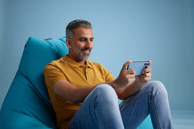A portrait of an Arab Saudi Gulf man wearing casual attire sitting on a chair among blue flowers, with various gestures and movements, against a blue background.