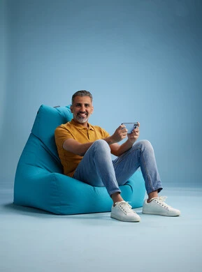 A portrait of an Arab Saudi Gulf man wearing casual attire sitting on a chair among blue flowers, with various gestures and movements, against a blue background.