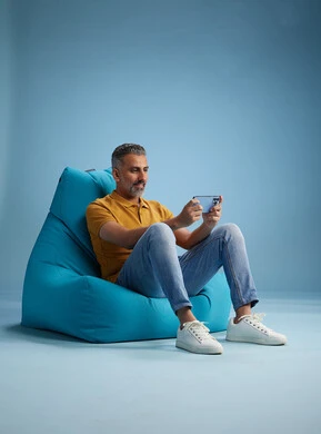 A portrait of an Arab Saudi Gulf man wearing casual attire sitting on a chair among blue flowers, with various gestures and movements, against a blue background.