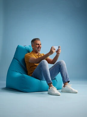 A portrait of an Arab Saudi Gulf man wearing casual attire sitting on a chair among blue flowers, with various gestures and movements, against a blue background.