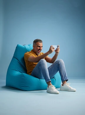 A portrait of an Arab Saudi Gulf man wearing casual attire sitting on a chair among blue flowers, with various gestures and movements, against a blue background.