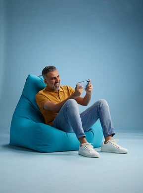 A portrait of an Arab Saudi Gulf man wearing casual attire sitting on a chair among blue flowers, with various gestures and movements, against a blue background.