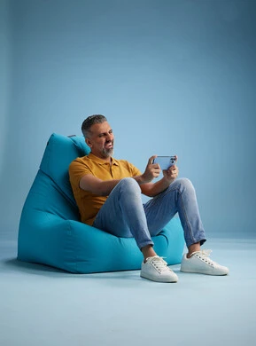 A portrait of an Arab Saudi Gulf man wearing casual attire sitting on a chair among blue flowers, with various gestures and movements, against a blue background.