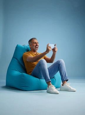 A portrait of an Arab Saudi Gulf man wearing casual attire sitting on a chair among blue flowers, with various gestures and movements, against a blue background.