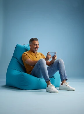 A portrait of an Arab Saudi Gulf man wearing casual attire sitting on a chair among blue flowers, with various gestures and movements, against a blue background.