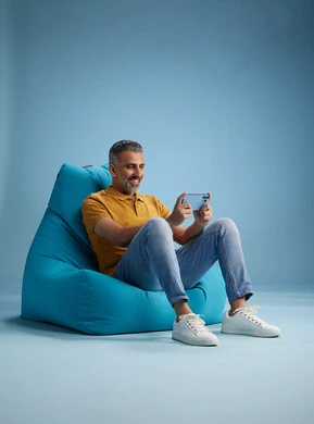 A portrait of an Arab Saudi Gulf man wearing casual attire sitting on a chair among blue flowers, with various gestures and movements, against a blue background.