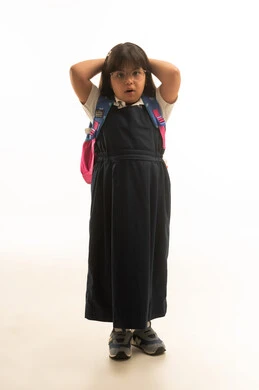 Arms behind the head, a small Arab Gulf Saudi girl with special needs wearing a gray school uniform looking at the camera, full body, portrait with a white background.