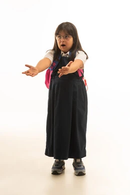 متلازمة داون , بنت صغيرة عربية خليجية سعودية من ذوي الهمم ترتدي الزي المدرسي الموحد باللون الرمادي تفرد الذراعين امام الكاميرا اشارة الى طلب شئ ما , الجسم بالطول الكامل , بورتريه خلفية بيضاء