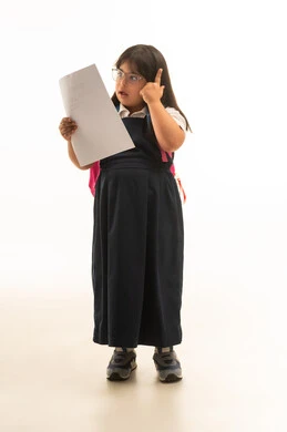 بنت صغيرة عربية خليجية سعودية من ذوي الهمم ترتد زي المدرسة الموحد باللون الرمادي تنظر الى الاوراق الدراسية , حمل الحقيبة المدرسية الملونة , الجسم بالطول الكامل , بورتريه خلفية بيضاء