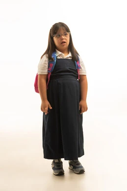 الوقوف امام الكاميرا , النظر الي شئ ما , بنت صغيرة عربية خليجية سعودية تعاني من متلازمة داون ترتدي الزي المدرسي الموحد باللون الرمادي , الجسم بالطول الكامل , بورتريه خلفية بيضاء