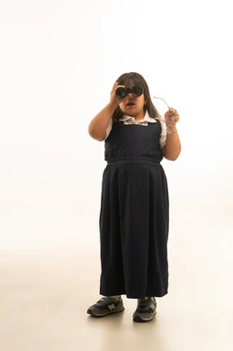 Looking towards the camera using a zoom lens, a young Arab Gulf Saudi girl wearing a gray school uniform holding a zoom lens, full body, portrait with a white background.