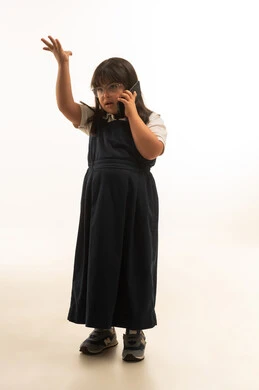 Raising the hand up during a phone call, gestures of rejection and nervousness, a small Arab Gulf Saudi girl with determination wearing a gray school uniform talking on a mobile phone, full-body, portrait with a white background.