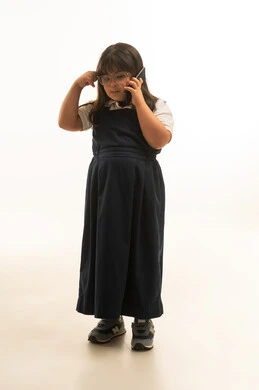 Scratching the head while talking on a mobile phone, a young Saudi Arabian Gulf girl with Down syndrome is talking on the phone, gestures of confusion and questioning, full-body, portrait with a white background.