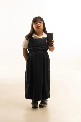 عرض شاشة هاتف محمول سوداء فارغة للكاميرا , بنت عربية خليجية سعودية صغيرة من ذوي الاحتياجات الخاصة ترتدي الزي المدرسي الموحد لون رمادي , الجسم بالطول الكامل , بورتريه خلفية بيضاء