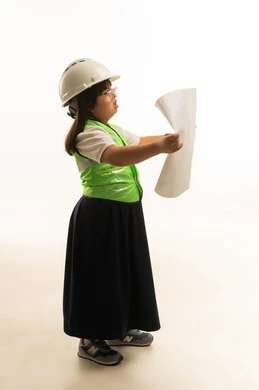 التساؤل اثناء التفكير العميق في المخطط الهندسي , بنت صغيرة عربية خليجية سعودية ترتدي الزي المدرسي الموحد لون رمادي مع السترة الواقية و خوذة الامان , حمل الرسومات الهنسية المعمارية , الجسم بالطول الكامل , بورتريه خلفية بيضاء