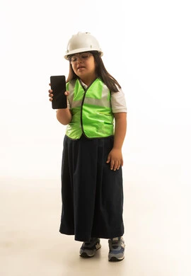 Looking at the empty black mobile phone screen, a small Arab Gulf Saudi girl with Down syndrome is wearing a reflective vest with a gray uniform, standing in front of the camera, full body, white background.
