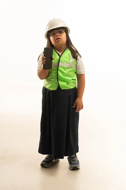 A small Arab Gulf Saudi girl with Down syndrome wearing a gray school uniform with a protective jacket, showing a blank black mobile phone screen to the camera, full body, portrait with a white background.