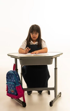 التلوين بالقلم الاسود , بنت صغيرة عربية خليجية سعودية من ذوي الهمم ترتدي زي مدرسة موحد لون كحلي تنظر الى كتاب التلوين , الجسم بالطول الكامل , بورتريه خلفية بيضاء