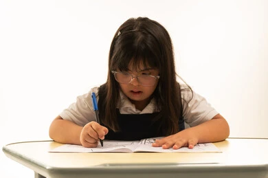 عمل انشطة مسلية اثناء اليوم الدراسي , بنت صغيرة عربية خليجية سعودية من ذوي الهمم ترتدي زي مدرسة موحد لون كحلي تجلس امام طاولة الرسم و التلوين , انشطة ابداعية , بورتريه مقرب , خلفية بيضاء