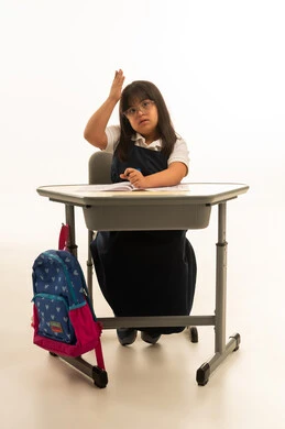 رفع كف اليد لاعلى علامة على الطلب و الاستئذان , بنت صغيرة عربية خليجية سعودية من متلازمة داون ترتدي الزي المدرسي الموحد لون كحلي ,النظر الى الكاميرا , الجسم بالطول الكامل , بورتريه خلففية بيضاء