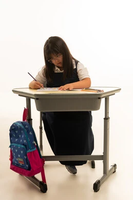 Looking at the drawing on the school desk, a small Arab Gulf Saudi girl with Down syndrome wearing a navy blue school uniform is drawing with colored pencils, full-body, portrait with a white background.