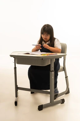 بنت صغيرة عربية خليجية سعودية تعاني من متلازمة داون ترتدي الزي الموحد لون كحلي تمسك القلم الرصاص , النظر الى الكراسة على مقعد المدرسة , الجسم بالطول الكامل , بورتريه خلفية بيضاء