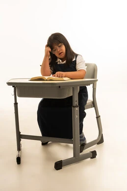 التفكير العميق و التركيز اثناء اليوم الدراسي , بنت صغيرة عربية خليجية سعودية من ذوي الهمم ترتدي الزي المدرسي الموحد تجلس داخل الفصل المدرسي , الجسم بالطول الكامل , بورتريه خلفية بيضاء