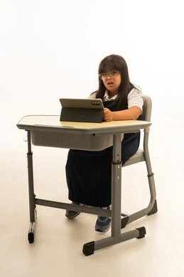 Looking at something, a small Arab Gulf Saudi girl with Down syndrome using a tablet in the educational process, sitting inside the classroom, portrait with a white background, full body.