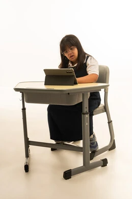 متابعة الدروس اليومية على الجهاز اللوحي , بنت صغيرة عربية خليجية سعودية من ذوي الهمم ترتد زي المدرسة الكحلي تجلس داخل الفصل الدراسي , الجسم بالطول الكامل , بورتريه خلفية بيضاء