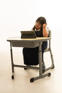 وضع اصبع السبابة على الرأس اشارة الى التفكير العميق , بنت صغيرة عربية خليجية سعودية تعاني من متلازمة داون ترتدي الزي المدرسي الكحلي , الجلوس على مقاعد الفصل الدراسي , استخدام الاجهزة اللوحية الحديثة في التعليم , بورتريه الجسم بالطول الكامل , خلفية بيضاء