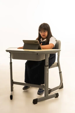 النظر الى شاشة الجهاز اللوحي , بنت عربية خليجية سعودية صغيرة تعاني من متلازمة داون ترتد الزي المدرسي تجلس داخل الفصل الدراسي , استخدام الاجهزة التقنية الحديثة داخل المدارس , الجسم بالطول الكامل , بورتريه خلفية بيضاء