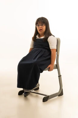 الانصات الى المعلمة داخل الفصل الدراسي , بنت عربية خليجية سعودية صغيرة من اصحاب متلازمة داون ترتدي زي المدرسة الكحلي تجلس على المقعد , الجسم بالطول الكامل , بورتريه خلفية بيضاء