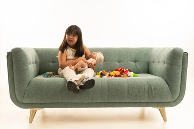 النظر الى شئ ما , بنت عربية خليجية سعودية صغيرة مناصحاب متلازمة داون تحمل الدمية الصغيرة ,الجلوس بجانب العاب تنمية المهارات الذهنية , الجسم بالطول الكامل , بورتريه خلفية بيضاء