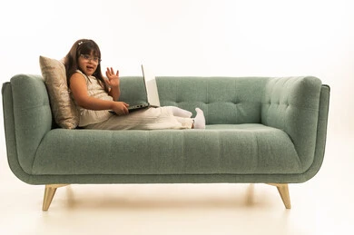 Waving with the hand is a sign of peace and greeting, a Saudi Arabian Gulf girl with Down syndrome holding a laptop, gestures of happiness and a smile in front of the camera, full-body, portrait with a white background.