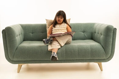 القراءة بصوت مرتفع , بنتعربية خليجية سعودية من ذوي الاحتياجات الخاصة ترتدي الزي الكاجوال , الجلوس على الاريكة الرمادية اثناء القراءة , بورتريه خلفية بيضاء , الجسم بالطول الكامل