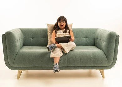 Looking at the camera, a Saudi Arabian Gulf girl with Down syndrome holding a tablet, sitting with one leg crossed over the other, portrait with a white background, full body.