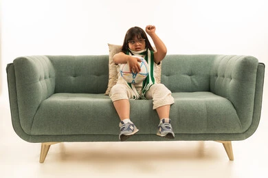 رفع قبضة اليد لاعلى اشارة الى التشجيع , بنت صغيرة عربية خليجية سعودية من ذوي الهمم ترتدي الزي الكاجوال تمسك كرة القدم , النظر الى شئ ما , الجسم بالطول الكامل , بورتريه خلفية بيضاء