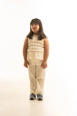 بنت صغيرة من ذوي الهمم عربية خليجية سعودية ترتدي الزي الكاجوال لون البيج , النظر الي شئ ما , الجسم بالطول الكامل , بورتريه خلفية بيضاء , ايماءات التساؤل و الحيرة