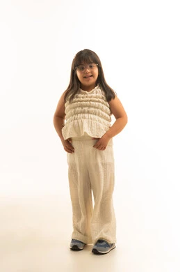 النظر الى الكاميرا , الابتسامة البريئة , بنت صغيرة من ذوي الهمم عربية خليجية سعودية ترتدي الزي الكاجوال , اللون البيج , الجسم بالطول الكامل , بورتريه خلفية ببيضاء