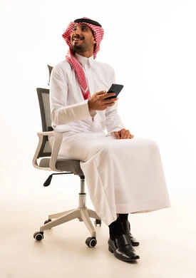 رجل سعودي يحمل هاتفا ذكيا جالسا على كرسي مكتب رجل سعودي يحمل هاتفا ذكيا جالسا على كرسي مكتب