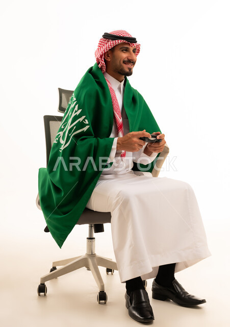 رجل سعودي يمسك جهاز تحكم ألعاب مع العلم الوطني