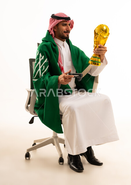 رجل سعودي يحمل كأس العالم وجهاز تحكم ألعاب
