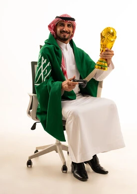 شاب سعودي بالزي التقليدي يحمل كأس ذهبية وجهاز ألعاب