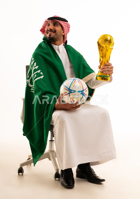 رجل سعودي يحمل كرة قدم وكأس مع العلم